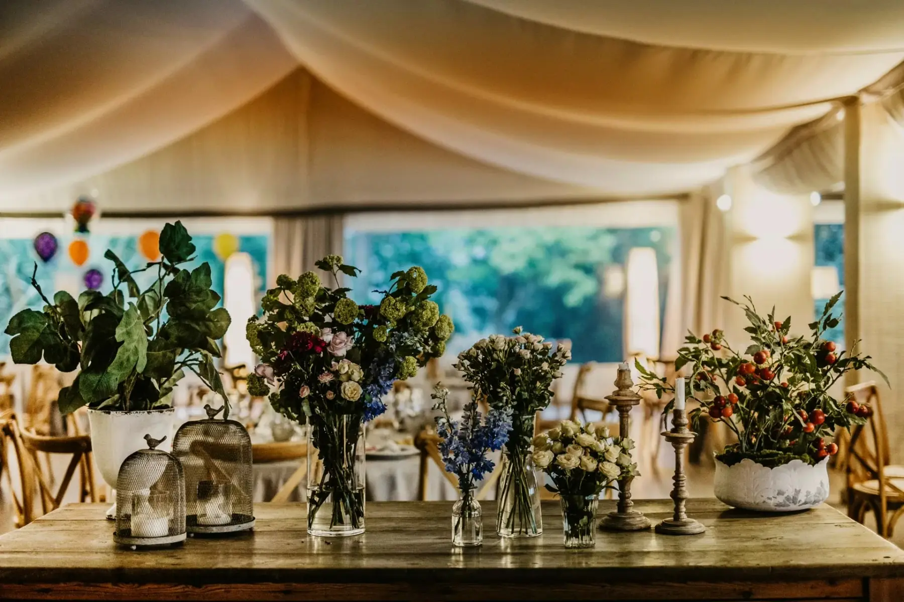 Una mesa de madera con jarrones de flores y velas bajo el techo de tela del salón